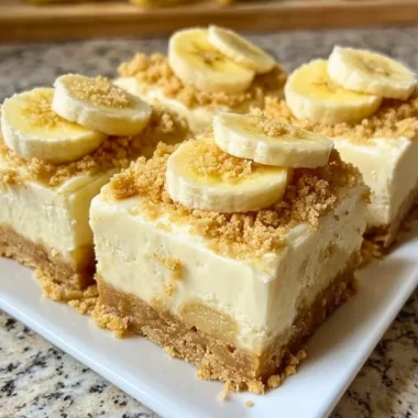 Delicious banana pudding cheesecake squares garnished with whipped cream and bananas.