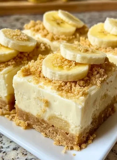 Delicious banana pudding cheesecake squares garnished with whipped cream and bananas.