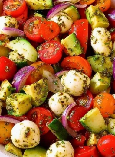 Tomato Cucumber Salad with Avocado, Mozzarella, and Basil Pesto served in a bowl