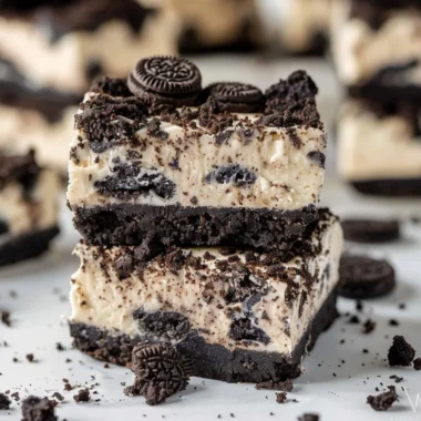 Delicious Oreo cheesecake bars topped with crushed Oreos on a white plate.