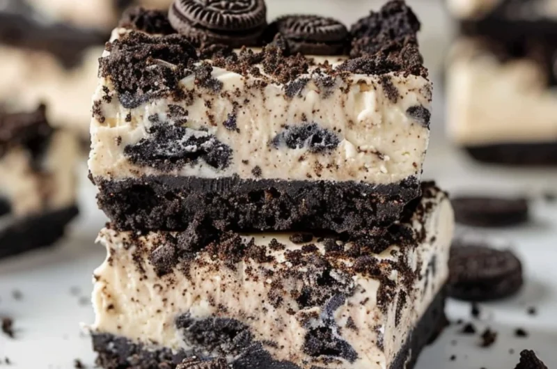 Delicious Oreo cheesecake bars topped with crushed Oreos on a white plate.