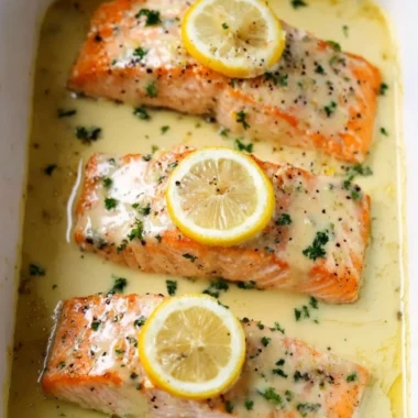 Plate of salmon topped with lemon cream sauce, garnished with herbs.