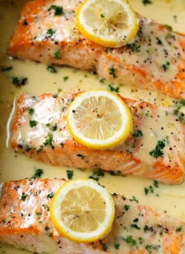 Plate of salmon topped with lemon cream sauce, garnished with herbs.