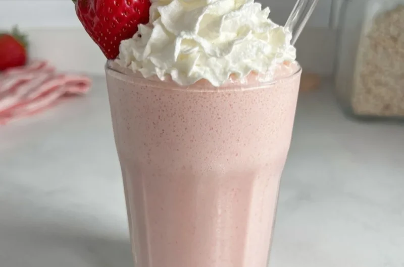 Strawberry protein shake in a glass with fresh strawberries on the side