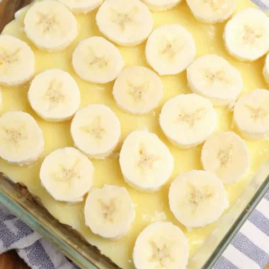 Slices of banana pudding poke cake topped with whipped cream and banana slices