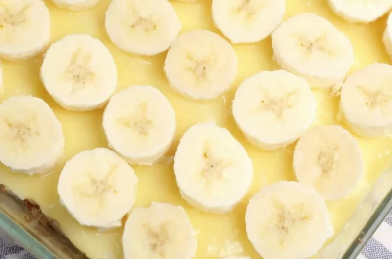 Slices of banana pudding poke cake topped with whipped cream and banana slices