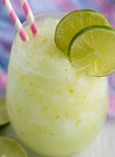 A refreshing Key Lime Cocktail garnished with lime and mint on a wooden table