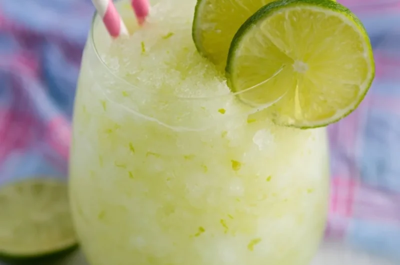 A refreshing Key Lime Cocktail garnished with lime and mint on a wooden table
