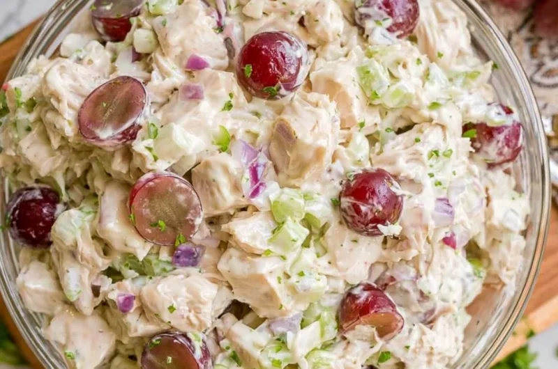 Shredded chicken salad with grapes in a bowl, garnished with herbs.