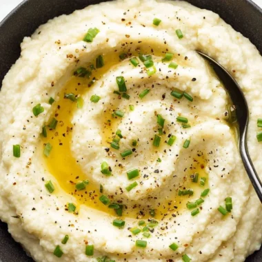 Bowl of creamy mashed cauliflower garnished with herbs on a rustic table