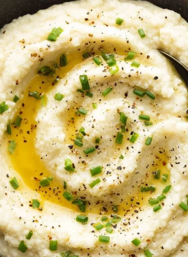 Bowl of creamy mashed cauliflower garnished with herbs on a rustic table