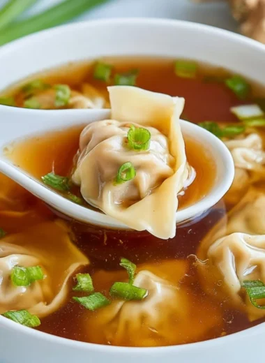 Bowl of steaming wonton soup with dumplings and green onions